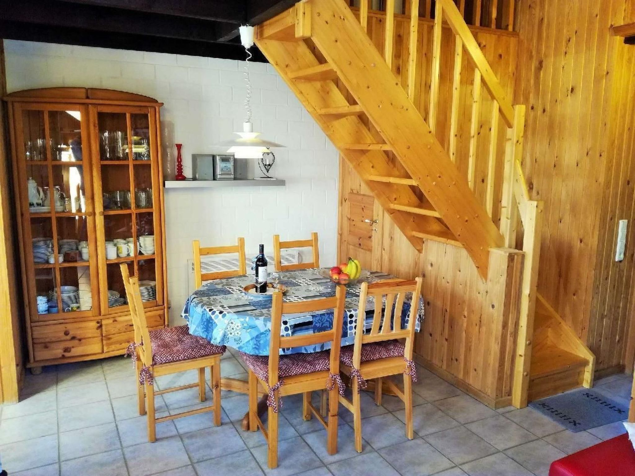 A wooden dining table with chairs, a cabinet with glass doors, and a wooden staircase.