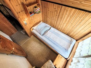 A small wooden room with a single bed, a small shelf with books, and a door. - Vacation home Mia by Interhome (Extertal)