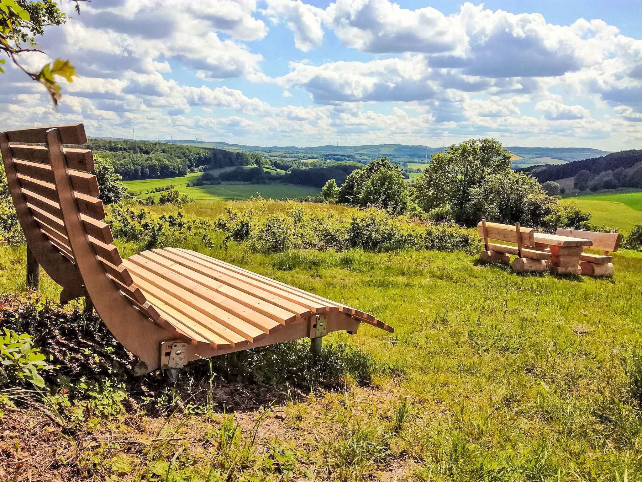 A wooden bench in a grassy field with a view of rolling hills and a clear sky.