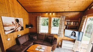 Ein gemütliches Zimmer mit Holzboden, einem braunen Sofa, einem Holztisch, einem Fernseher und einem Bücherregal.