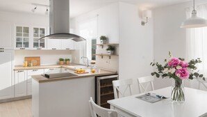 Eine moderne Küche mit weißen Schränken, einer zentralen Kochinsel und einem Essbereich mit weißem Tisch und Stühlen.