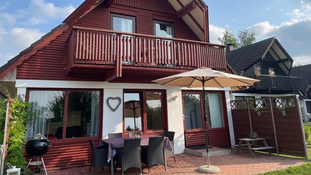 A two-story wooden house with a balcony, large windows, and a patio area with outdoor furniture. - Lisa am Silbersee  Silberseeblick by Interhome (Frielendorf)