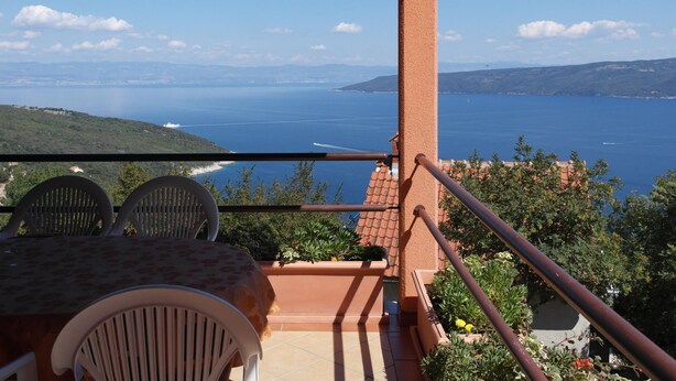 Een balkon met een tafel en stoelen, met uitzicht op een prachtig waterlandschap en heuvels in de verte.