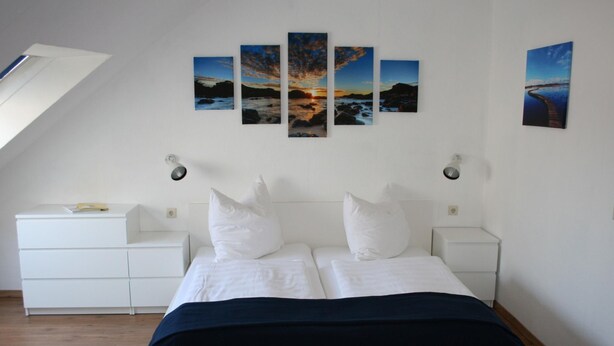 Ein Schlafzimmer mit einem Bett, weißen Nachttischen, einer weißen Kommode und einer geneigten Decke.