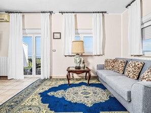 A living room with a sofa, patterned cushions, a table with a lamp, a blue patterned rug, and a view through a glass door. - Vacation home Sara by Interhome (Plomin)