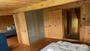 Ein Holzblockhaus-Interieur mit einem Bett, einem Schminktisch und einer Schiebetür zu einem Duschbereich.