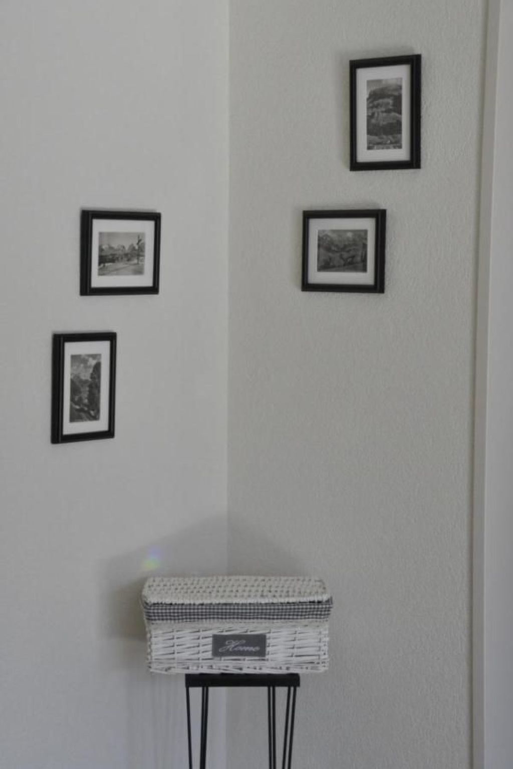 Eine Wand mit vier gerahmten Bildern und einem kleinen Korb auf einem Beistelltisch.