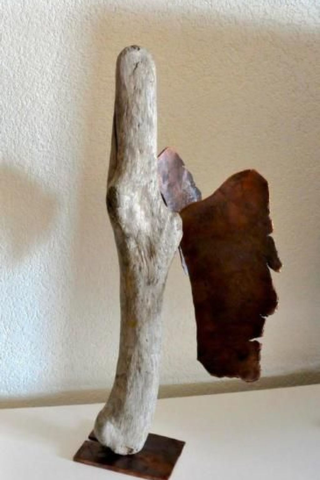 Una scultura dalla superficie ruvida con un elemento marrone, di forma irregolare, fissato ad essa.