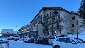 A multi-story hotel with balconies, a parking lot with several cars, and a clear sky.