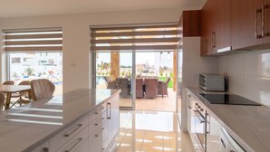 Une cuisine moderne dotée d’un grand îlot central, de portes-fenêtres coulissantes donnant sur un patio et offrant une vue sur une piscine et un espace de détente extérieur.