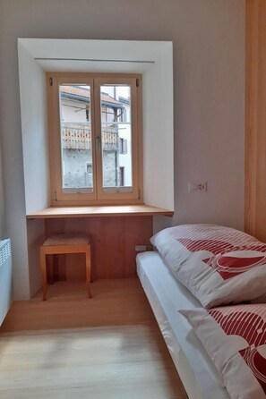 Une chambre à coucher avec un lit, un bureau en bois et une fenêtre donnant sur un immeuble.