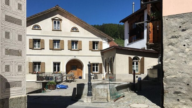 Ein traditionelles Gebäude mit symmetrischer Fassade, zahlreichen Fenstern mit Fensterläden und einem zentralen Eingang mit Bogen.