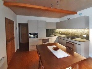 Une cuisine moderne avec une table à manger en bois, des armoires blanches et un pare-feu en pierre.
