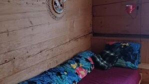 Une pièce de cabane en bois comprenant un lit, une petite table et un luminaire fixé au mur.