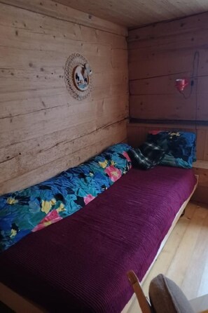 Ein Zimmer in einer Holzhütte mit einem Bett, einem kleinen Tisch und einer Wandleuchte.