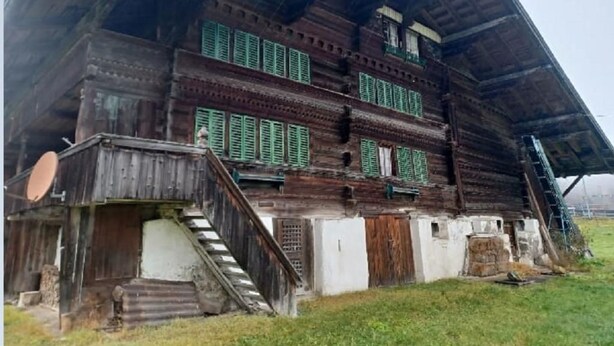 Un grand bâtiment rustique en bois, à plusieurs niveaux, avec des volets verts et un escalier menant à l’étage supérieur.