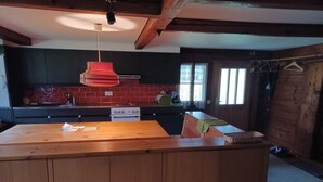 Une cuisine avec un îlot central en bois, un luminaire rouge suspendu et un mur de crédence en briques.