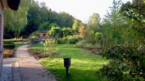 Een pad dat leidt naar een gebouw met een bakstenen gevel, omringd door weelderige begroeiing en een kleine brug.