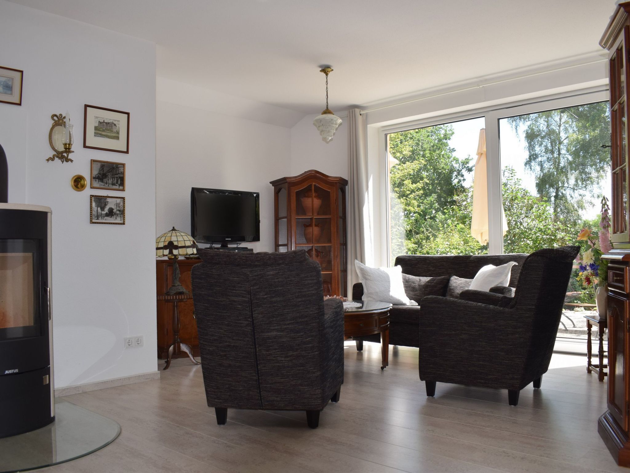 A living room with a TV, two armchairs, a wooden cabinet, and a large window with a view of trees.