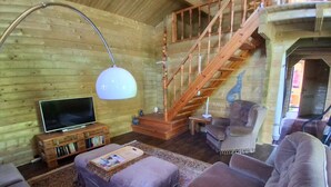 A cozy log cabin interior with a wooden staircase, a television, and a plush sofa. - Relax Chalet by Interhome (Sint-Annaland)