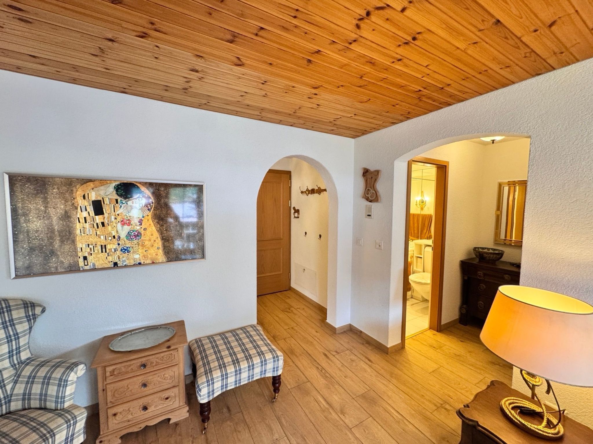 Ein Zimmer mit Holzboden, einem Gemälde an der Wand, einer Bank, einem Schminktisch und einer Lampe.
