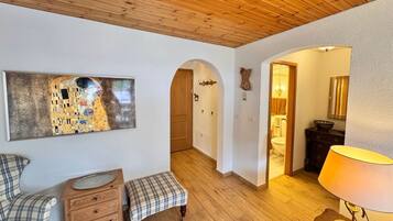 Ein Zimmer mit Holzboden, einem Gemälde an der Wand, einer Bank, einem Schminktisch und einer Lampe.