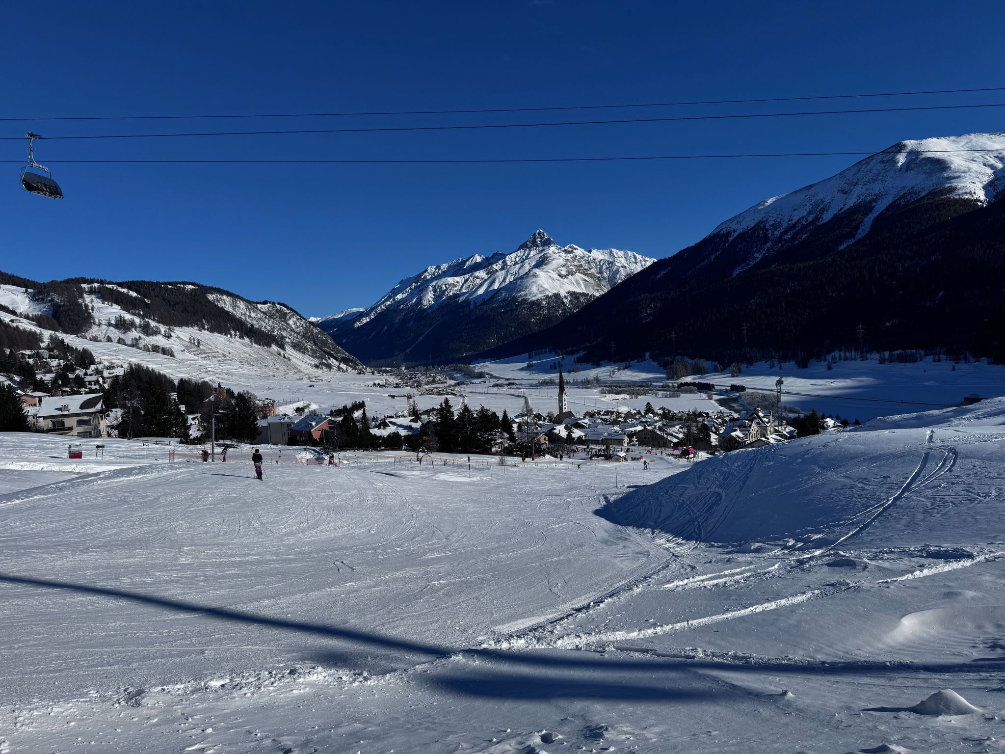 A snowy ski resort with a ski lift, a mountain backdrop, and a small town in the valley.