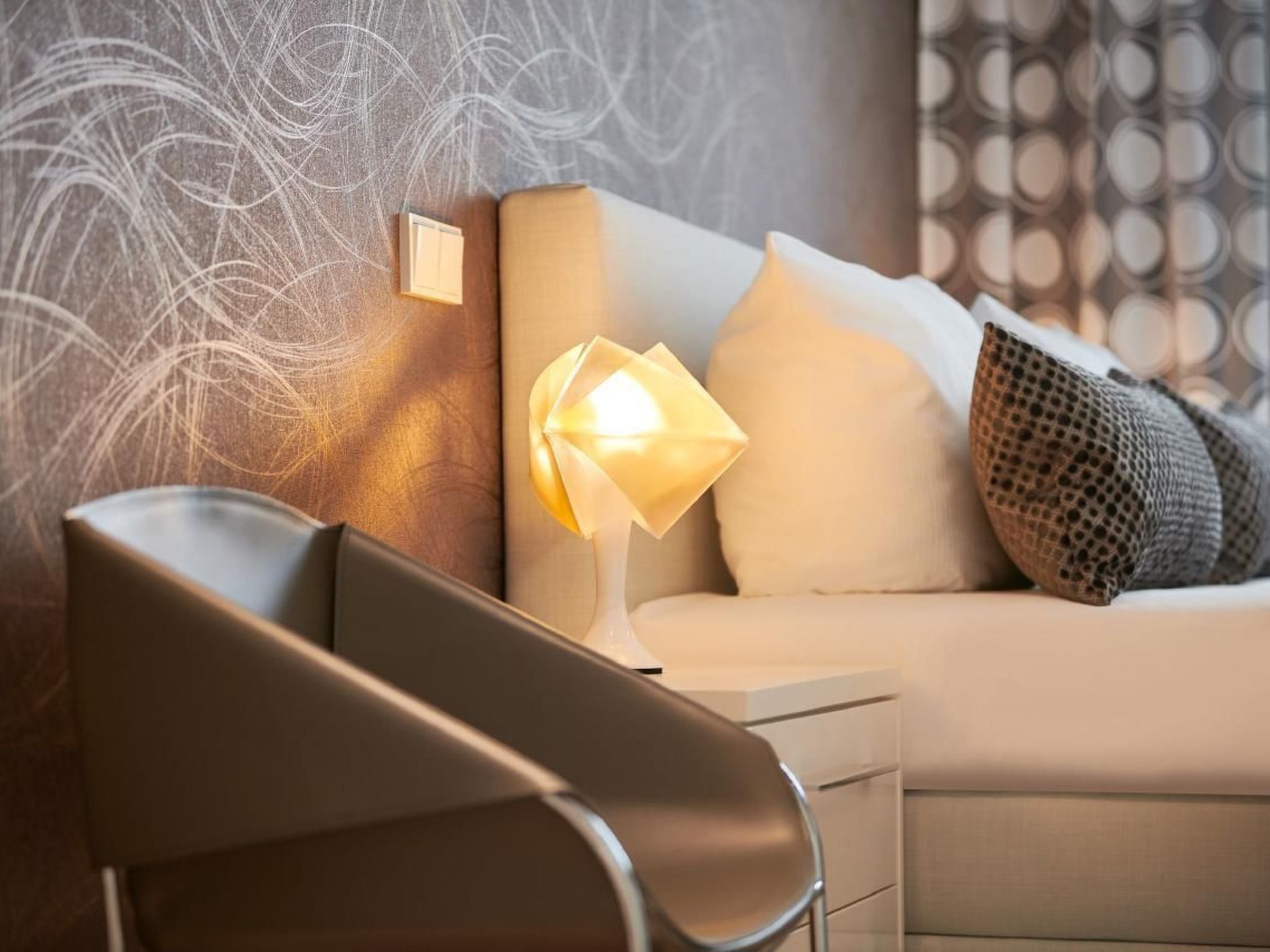 Quarto moderno com cama, mesa de cabeceira com abajur e uma cadeira.