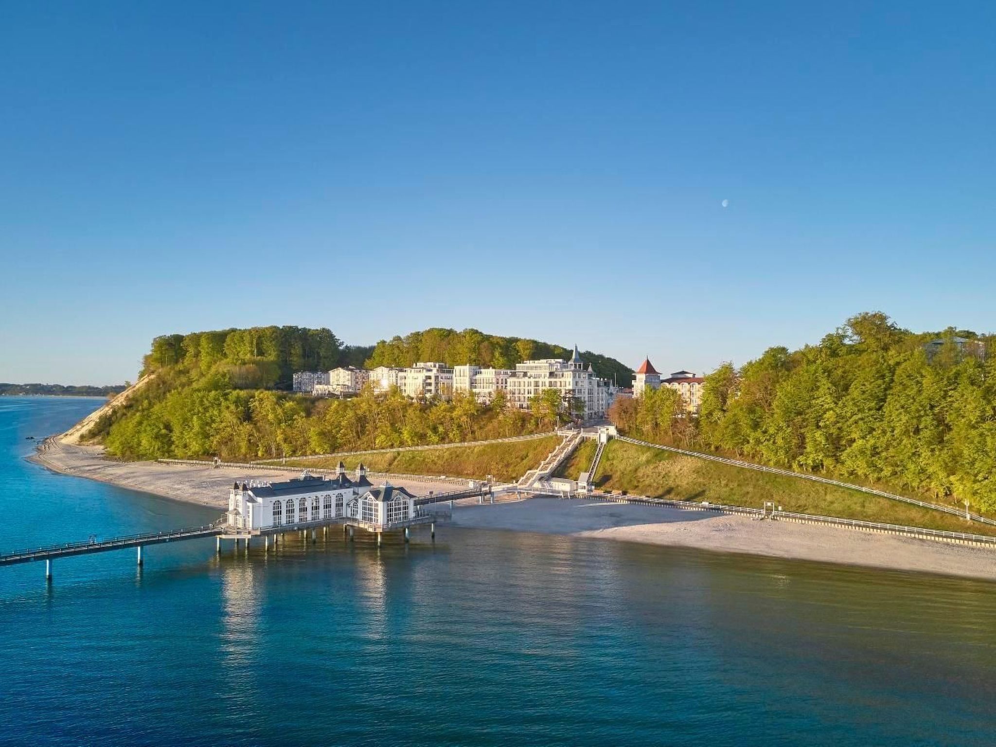 A coastal hotel with a large building, a pier, and a forested hill.