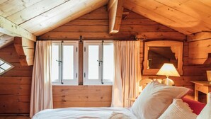 Un dormitorio rústico con cabaña de madera, una cama grande, una mesita de noche, una lámpara y una ventana con cortinas.