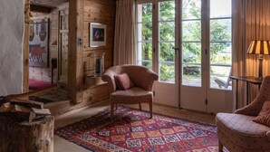 Una habitación acogedora con paredes de madera, un tapete estampado, un sillón de mimbre y un amplio ventanal con cortinas.