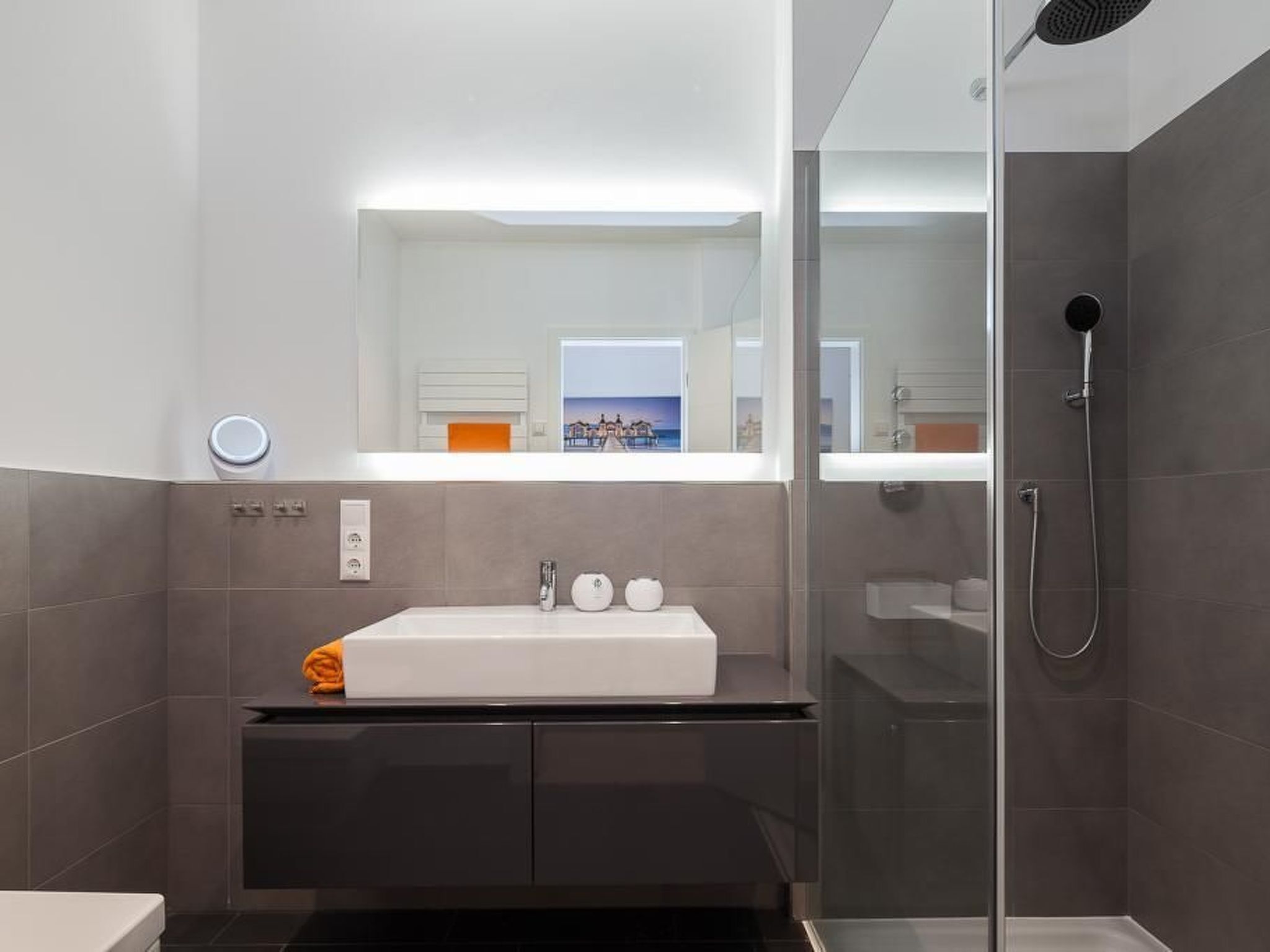 Une salle de bain moderne avec un grand miroir, un lavabo blanc et un espace douche.