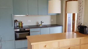 Une cuisine moderne avec des meubles de couleur bleu clair, un îlot central en bois, des appareils électroménagers en acier inoxydable et des luminaires suspendus.
