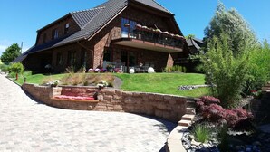 A two-story brick house with a balcony, a paved driveway, and a well-maintained garden with various plants and a small pond. - mit Terrasse in Sellin by Interhome (Ostseebad Sellin)