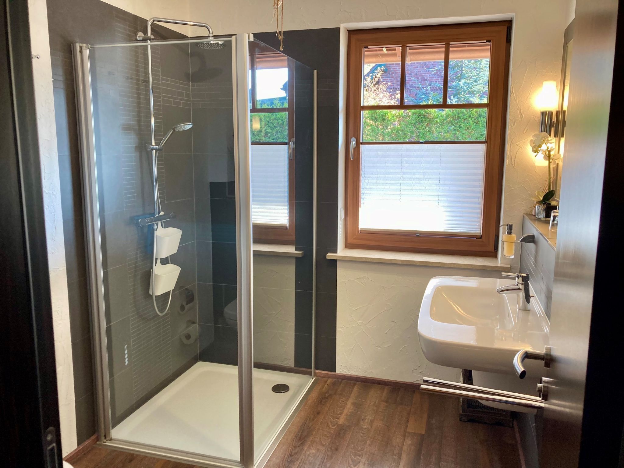 Un baño moderno con ducha de vidrio, lavamanos con espejo y ventana que deja entrar luz natural.