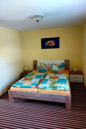 Een bed met een kleurrijke sprei, twee nachtkastjes met lampen, een ingelijst beeld aan de muur en een gestreept tapijt.