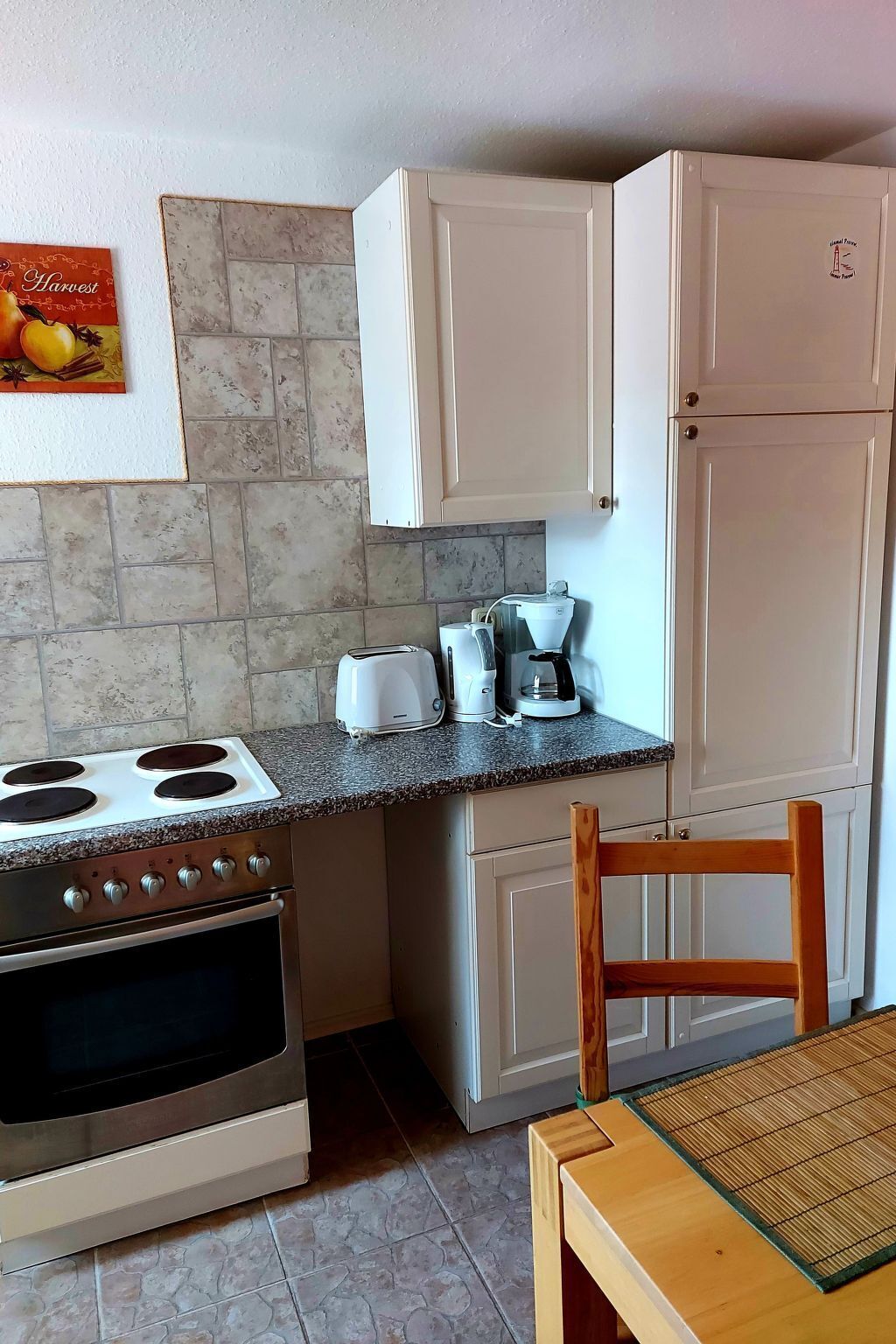 Eine kleine Küche mit Herd, Toaster, Kaffeemaschine und weißen Schränken.