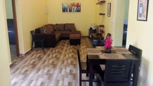 A living room with a brown sectional sofa, a dining table with chairs, and a wooden parquet floor. - Jeru Homes Ooty (Ooty)