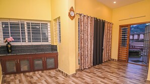 A room with a tiled floor, a window with blinds, a clock on the wall, and a door with a curtain. - Jeru Homes Ooty (Ooty)