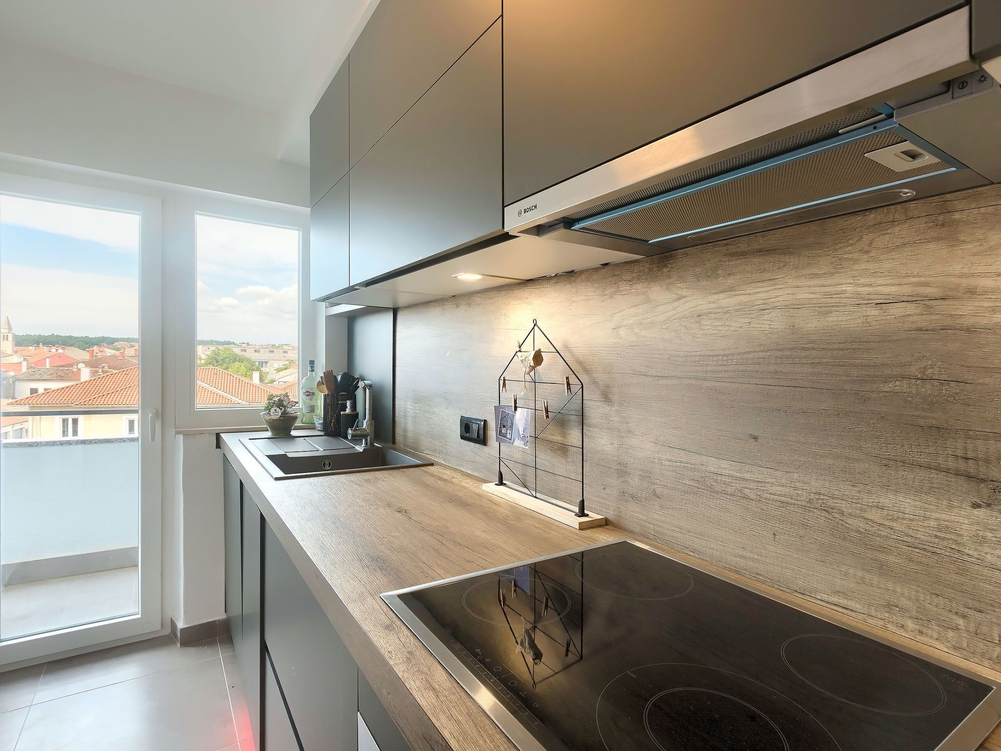 A modern kitchen with a large window, a built-in stove, and a wooden backsplash.