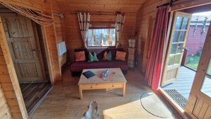 Et interiør af en træhytte med en sofa, et sofabord og en dør ud til det fri.