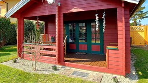 En rød træhytte med veranda, en grøn dør og en parabelfangst.