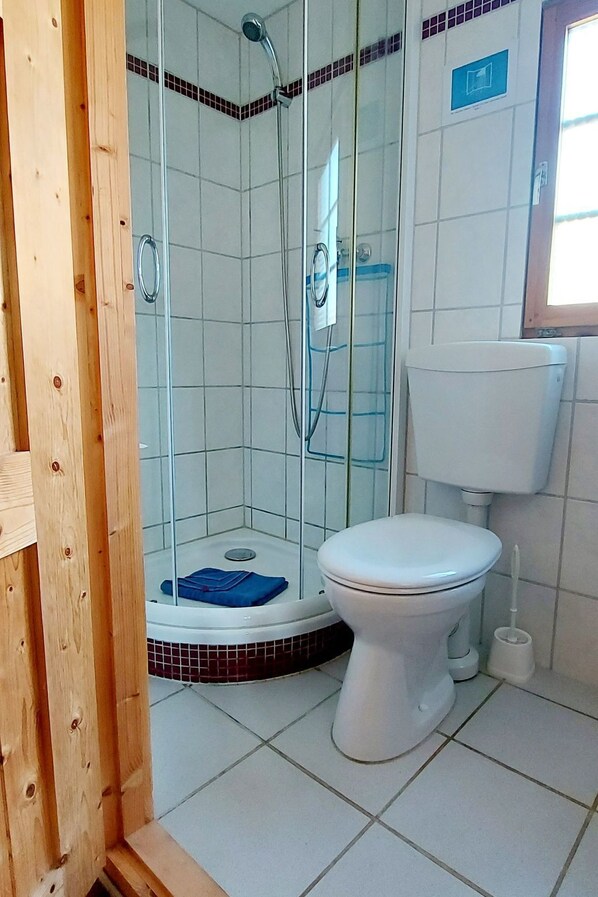 A bathroom with a glass-enclosed shower, a white toilet, and a tiled floor. - Blockhaus by Interhome (Born)