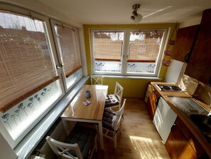 A compact kitchen with a wooden table, chairs, and a window with blinds. - Apartment Fewo1 by Interhome (Born)