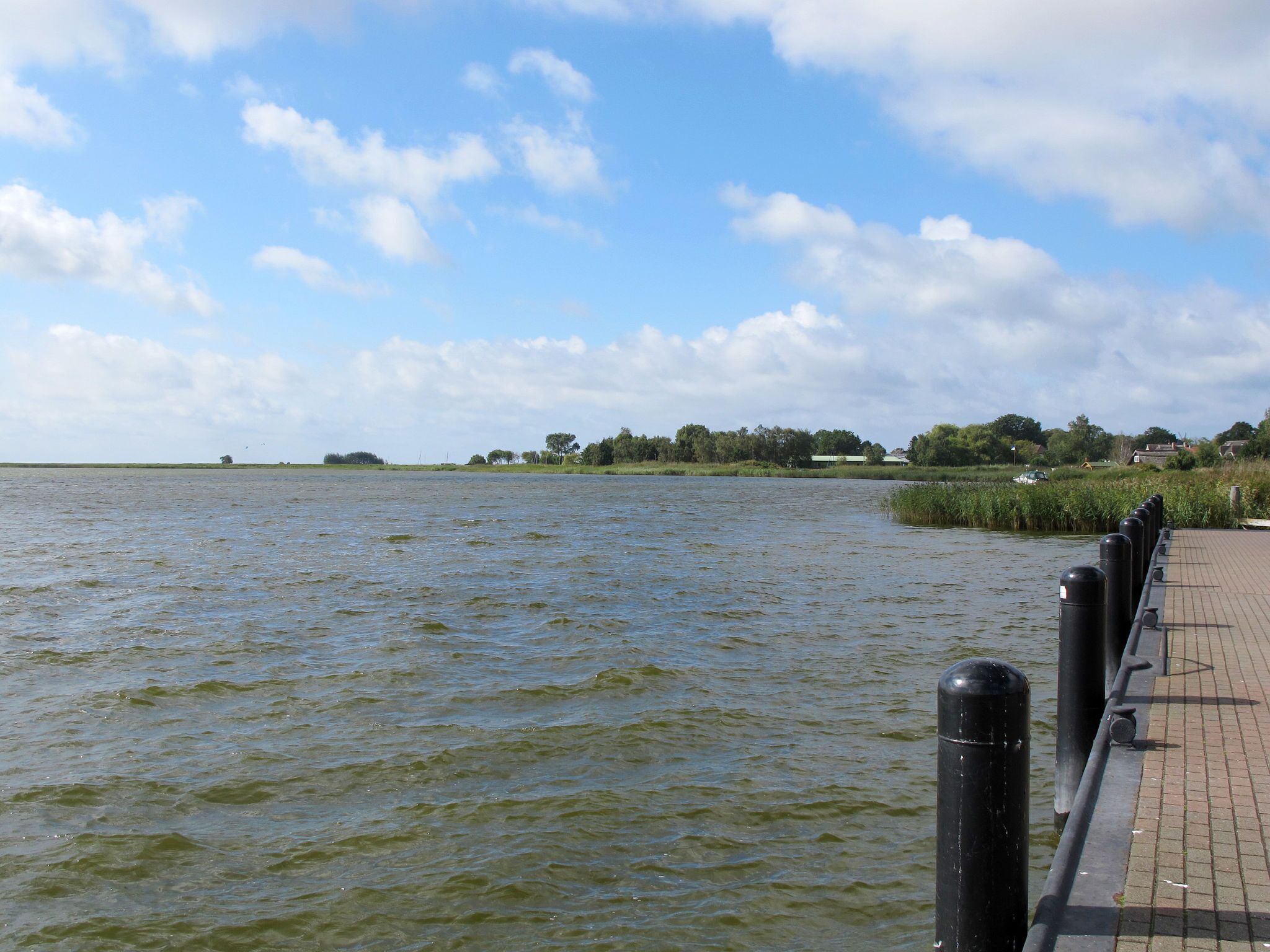 A calm river with a paved walkway and black bollards along the edge.
