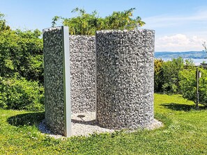A cylindrical stone structure with a metal frame, surrounded by greenery and a clear sky. - Riposo Impasse des Cerisiers by Interhome (Salavaux)