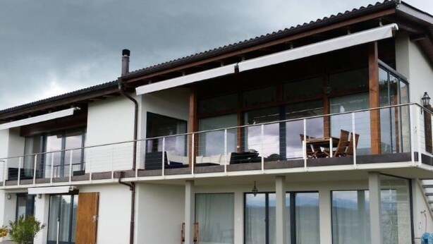 Et moderne hus i to etager med balkon, store vinduer og fladt tag.
