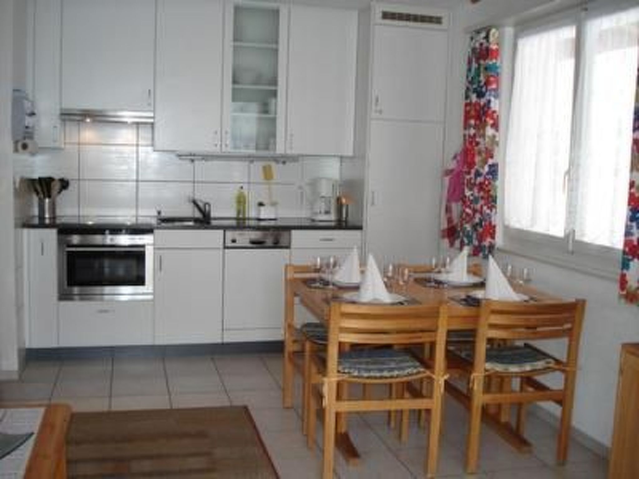A compact kitchen with white cabinets, a stove, and a dining area with wooden chairs and a table.