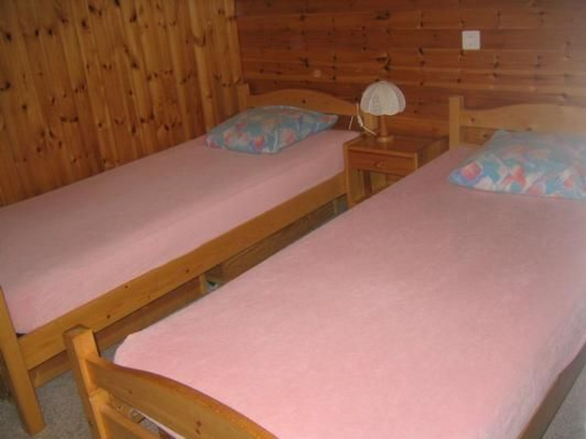 A small, wooden room with two single beds, each with a pink mattress and matching pillows.