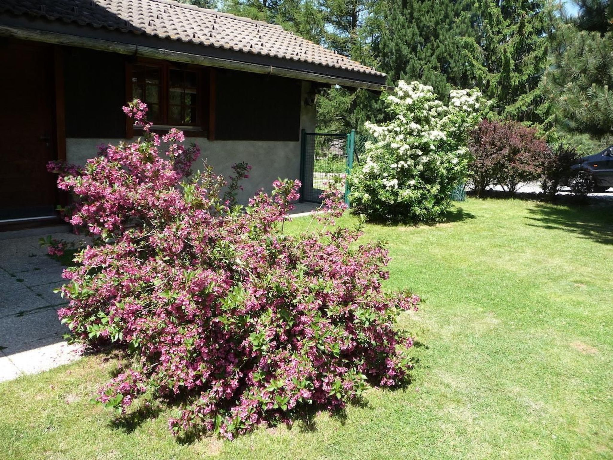 Un bâtiment doté d’un toit recouvert de tuiles, d’une pelouse bien entretenue et d’arbustes en fleurs.
